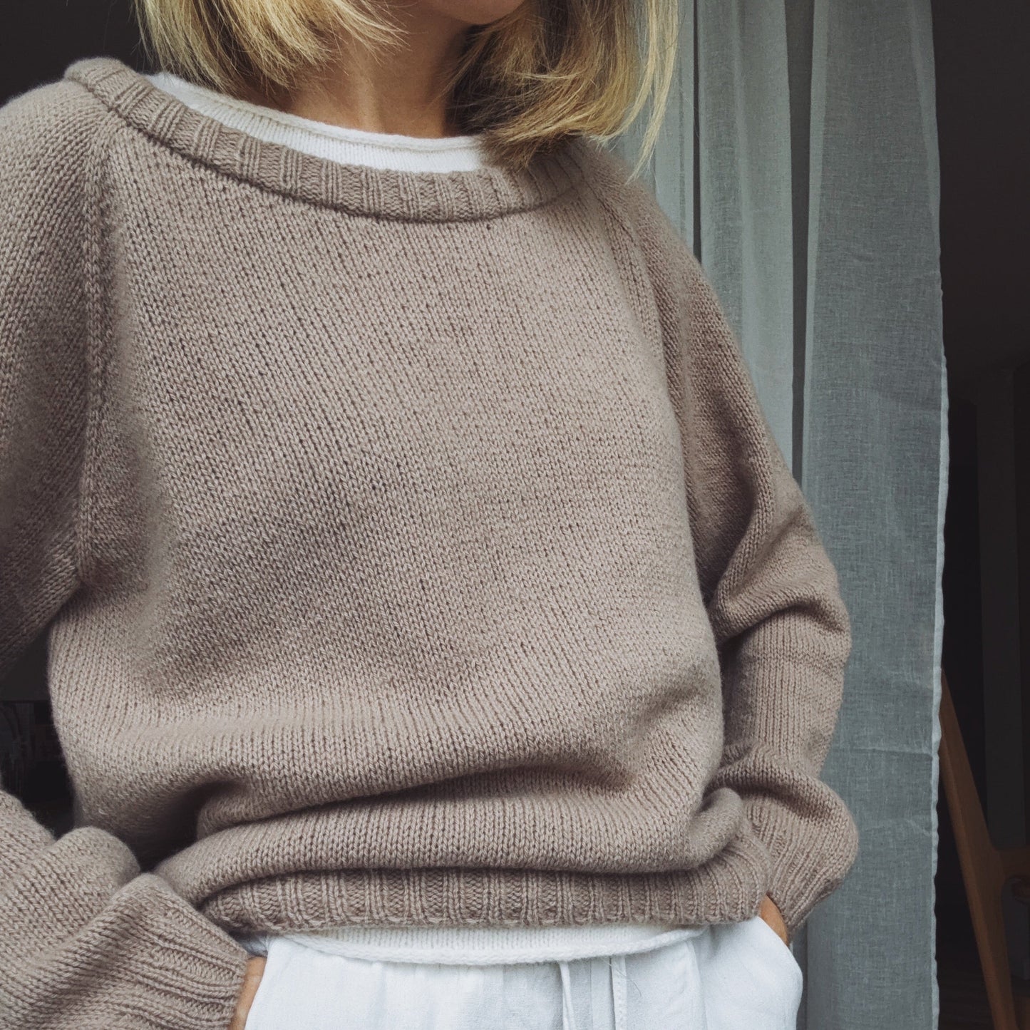 Person wearing a brown sweater and light blue pants with a neutral background
