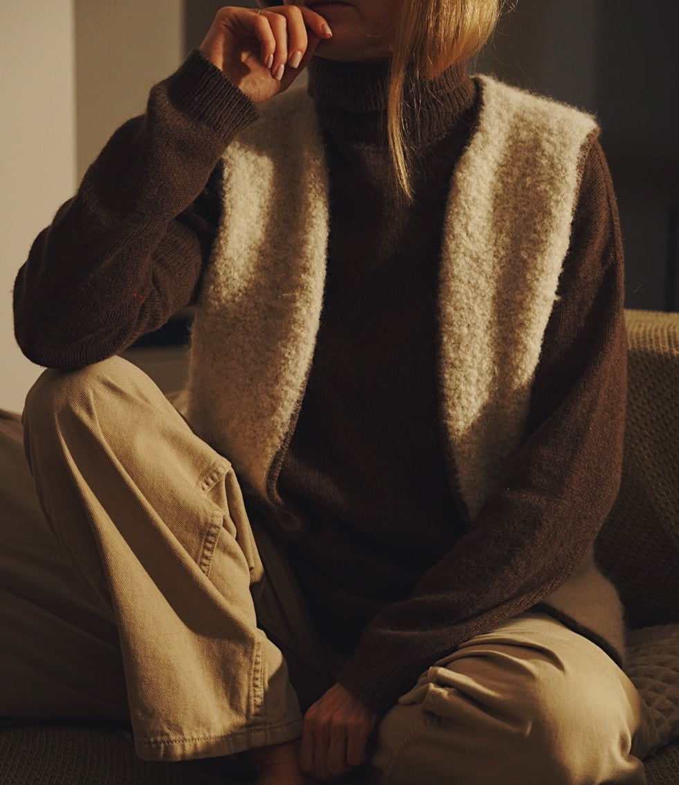 Person wearing a brown sweater with a patterned vest sitting on a couch.